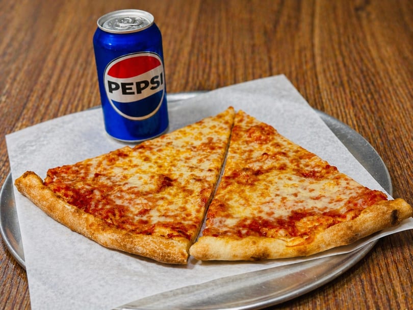 Two slices of cheese pizza and a Pepsi can on a metal tray with parchment paper.