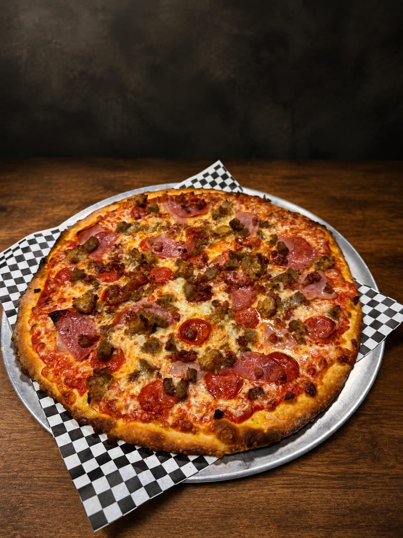 A large, hot meat lover's pizza with pepperoni, sausage, and ham on a metal pan.